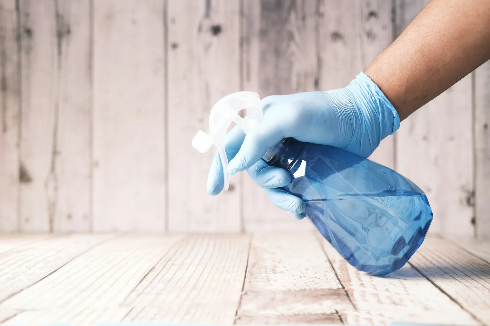 A gloved hand wiping a wood surface with a microfiber cloth